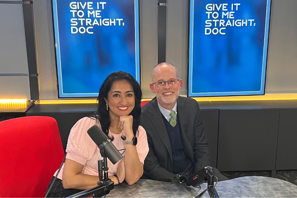 Anjalee Khemlani and Dr. Mark Moseley sit together in a studio-style setting, facing the camera. Khemlani is on the left and Moseley is on the right. Both appear engaged in conversation, with microphones visible in a podcast recording environment.