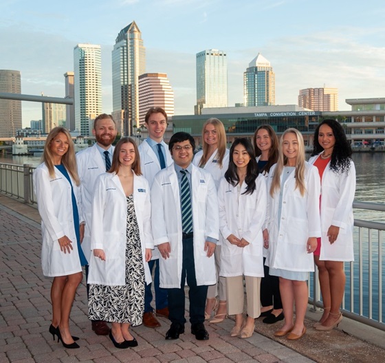 tgh pharmacy residency program residents pose for a group photo in their lab coats outside of tampa general hospital with tampa skyline in background