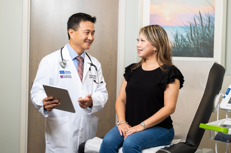 eugene shieh md holding a tablet and discussing its content with a female patient inside of a patient room at the tampa general mass general brigham cancer care clinic in palm beach gardens