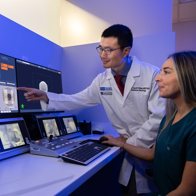 dr. scott chen and a female technician viewing imaging scans on a set of desktop monitors in a dimly lit room