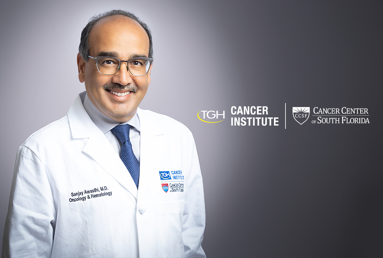 Dr. Sanjay Awasthi in a white lab coat standing beside the TGH Cancer Institute and Cancer Center of South Florida lockup logo