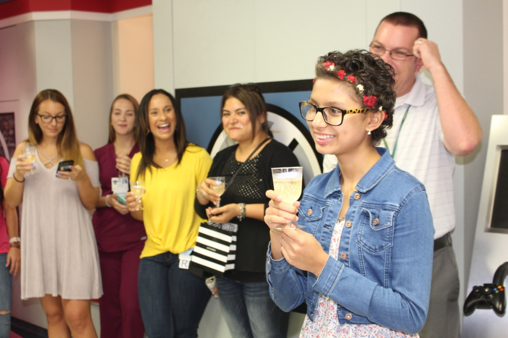 Group of people toasting to a teen girl ringing the chemo bell