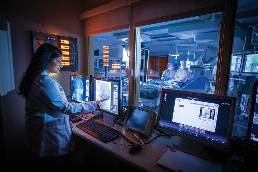 doctor observes monitors while surgeons perform endovascular neurosurgery procedure in the adjacent operating room