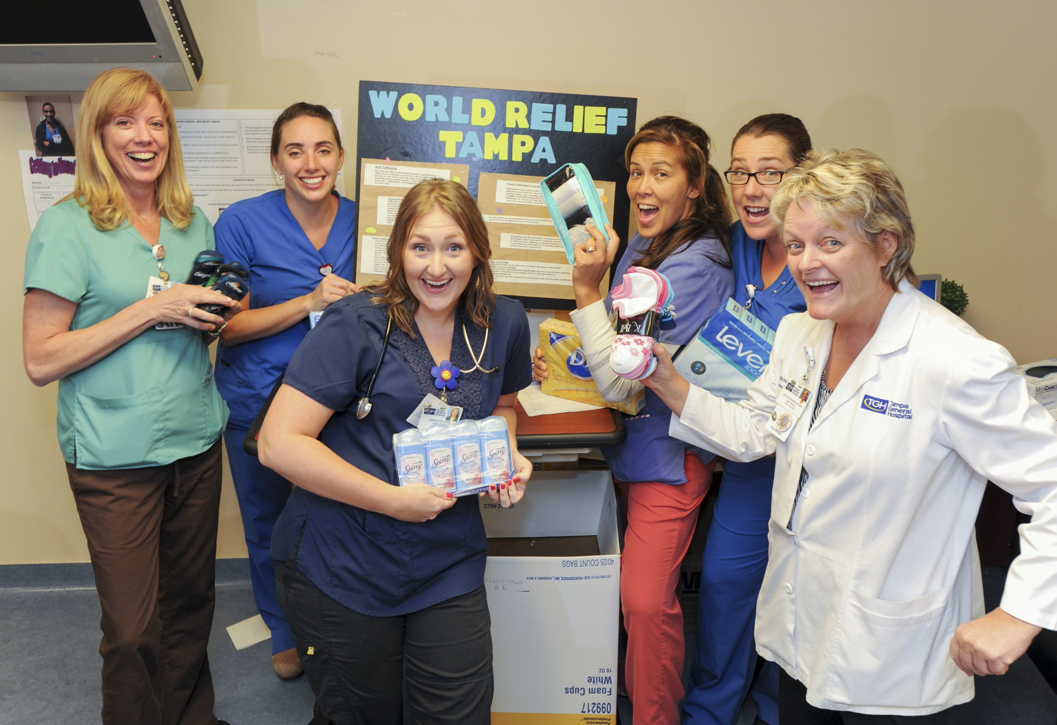 a group of female nurses and physician hold donation items for charity drive in front of a world relief tampa sign