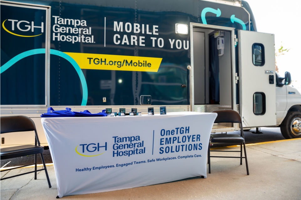 tgh mobile care to you bus parked behind a onetgh employer solutions table with chairs and swag