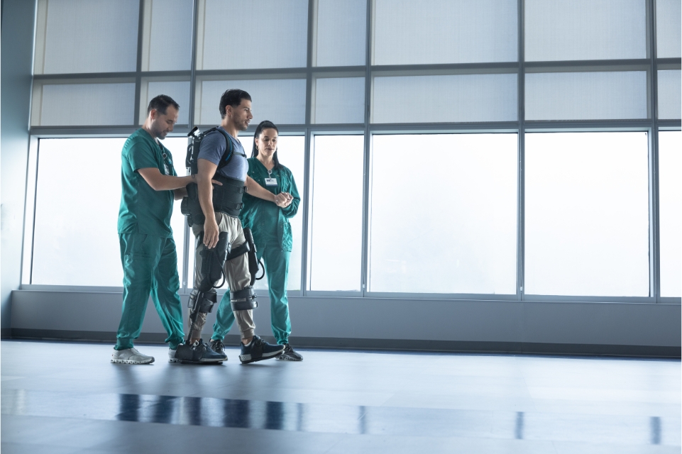 workers comp rehab patient taking steps in an exoskeleton with assistance from two nurses