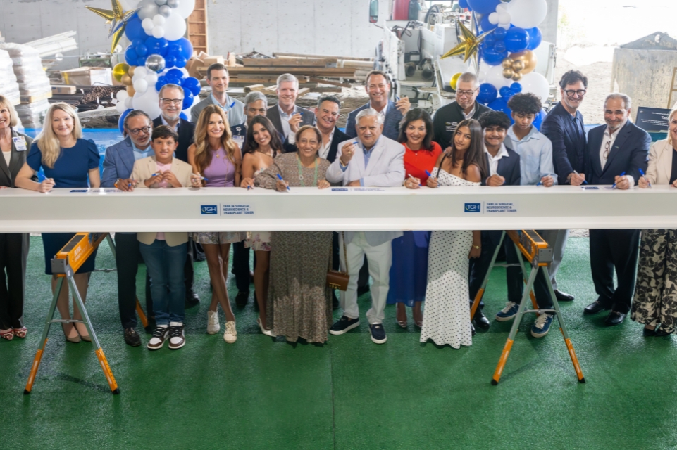 members of the taneja family foundation and tampa general hospital senior leadership team pose behind a beam they signed for the taneja tower topping out ceremony