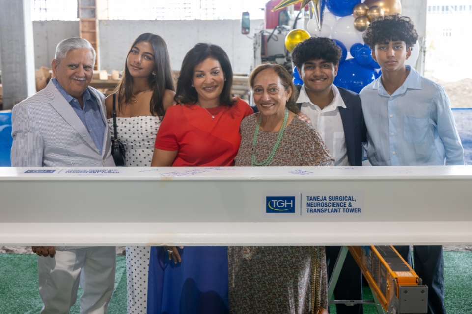 members of the taneja family pose behind a white beam with a tampa general hospital logo as part at the taneja tower topping out ceremony