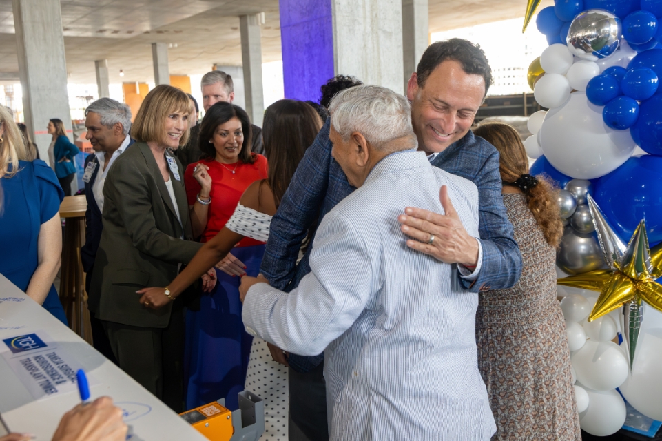 tgh ceo john couris and jugal taneja embrace at the taneja tower topping out ceremony with event guests and decorations in the background