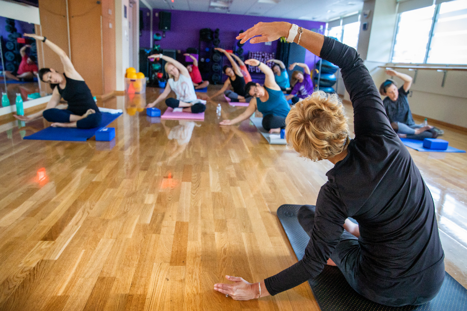 tgh fitness center group training class featuring female yoga instructor and group of students performing a pose while seated on the floor