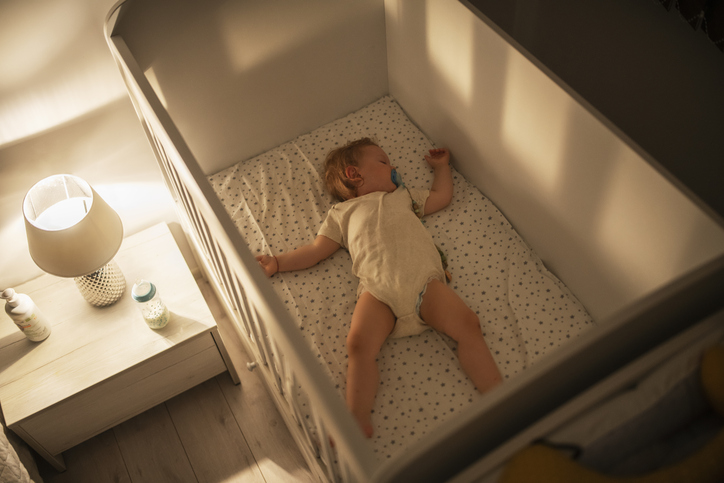 the abcs of safe sleep demonstrated by this image of a baby sleeping alone in his crib in a dimly lit nursery