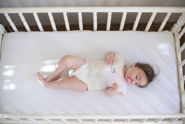 infant safe sleep image showing a baby sleeping on her back in her crib with a pacifier in her mouth