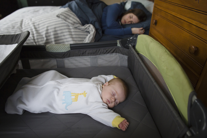 safe sleep for babies image showing a baby sleeping in a bassinet next to his mother sleeping in her bed